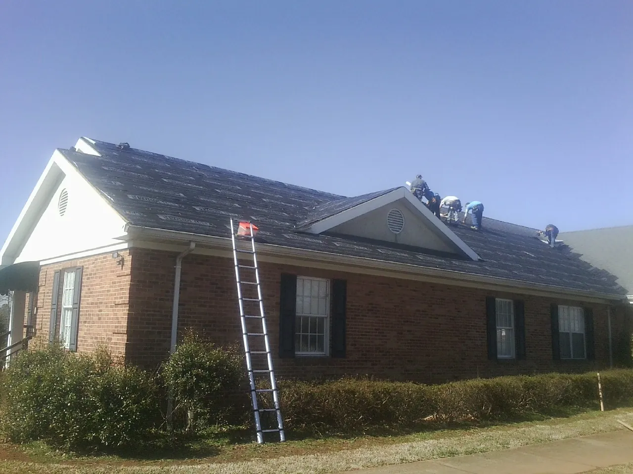 Crew tearing shingles off a brick ranch roof with a ladder set — Metal Roof Repair work by our crew in Shadyside