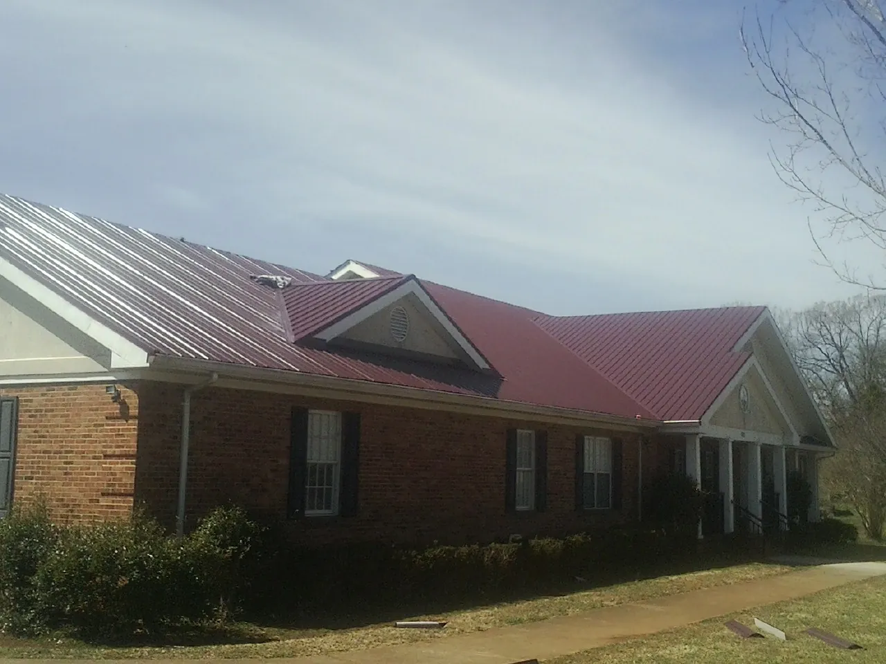 Red metal roof with gabled entries on a long brick building, from a Hail Damage Roof Repair job in Shadyside