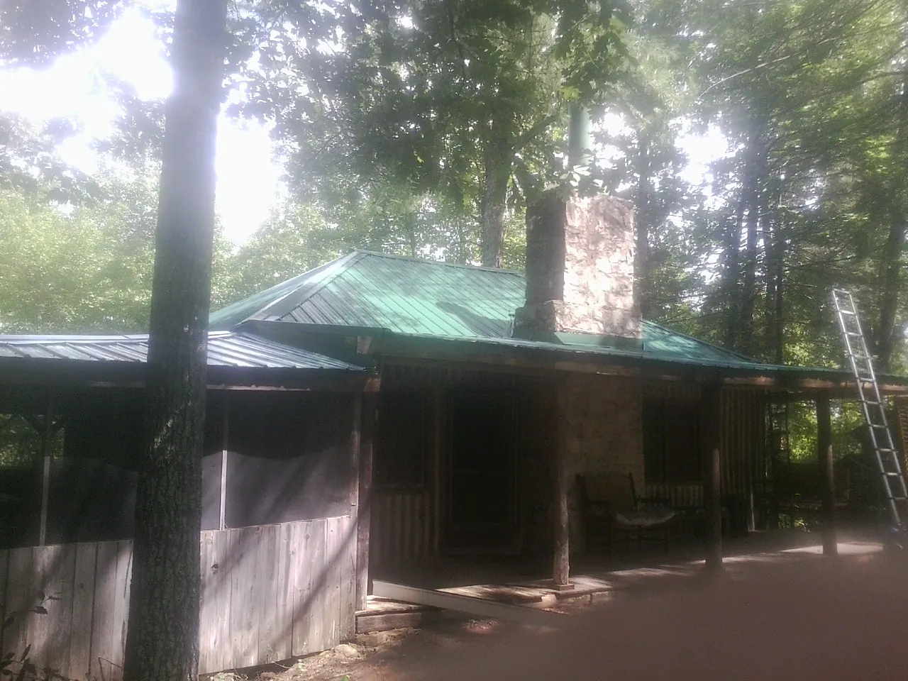 Green metal roof and stone chimney above a log cabin porch in Shadyside
