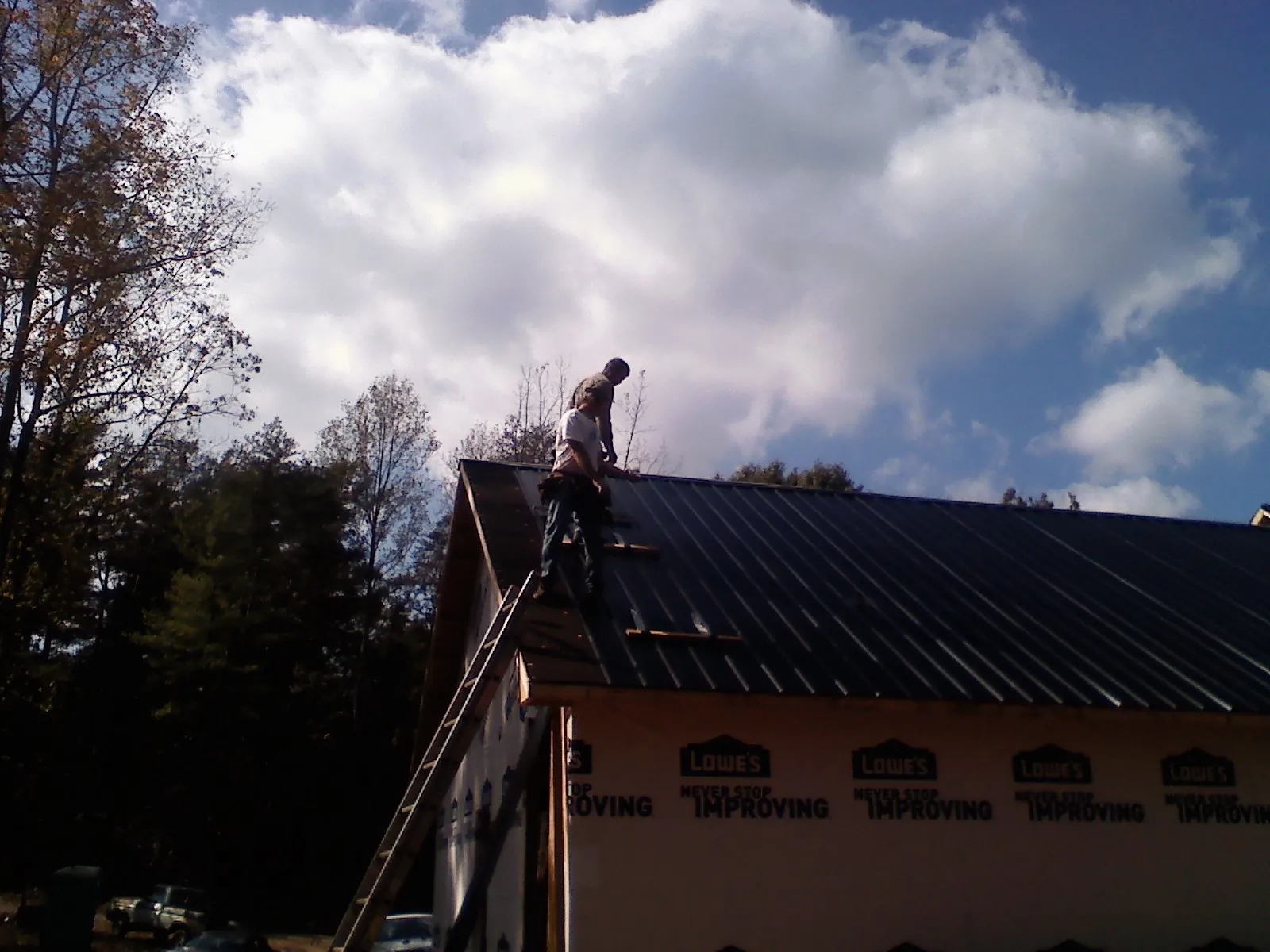Roofer fastening dark metal panels high against a cloudy sky, from a Roof Inspection job in Shadyside